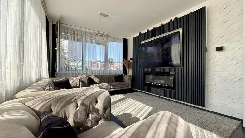 Helles Wohnzimmer mit modernem Sofa, integriertem Fernseher und dekorativer Wandverkleidung.
