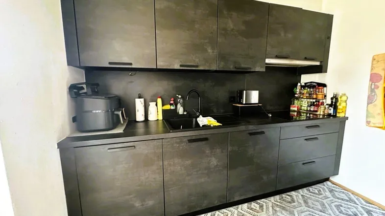 Moderne Küchenzeile mit dunklen Schränken, integrierter Spüle und Kochfeld, ideal für kompaktes Wohnen.