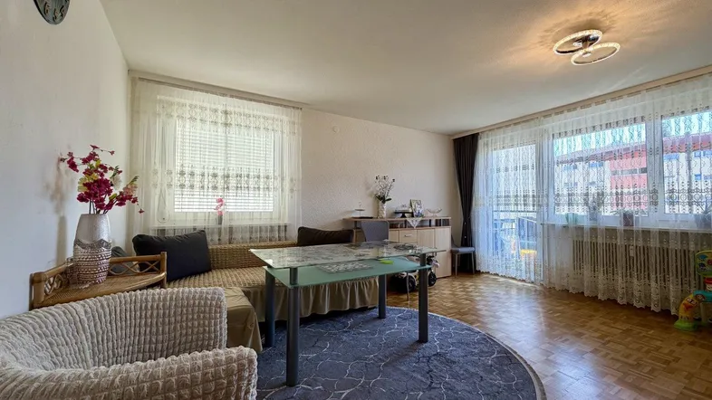 Helles Wohnzimmer mit Parkettboden, Sofa, Couchtisch und großen Fenstern.