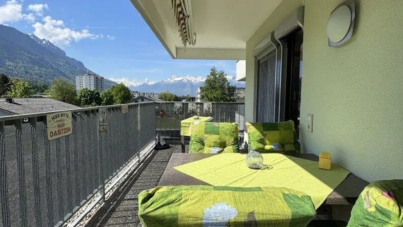 Heller Balkon mit Sitzgelegenheiten und beeindruckendem Bergblick unter blauem Himmel.