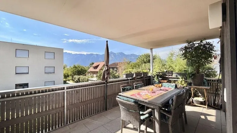 Geräumige Terrasse mit Esstisch und Stühlen, umgeben von Pflanzen und mit Bergblick.