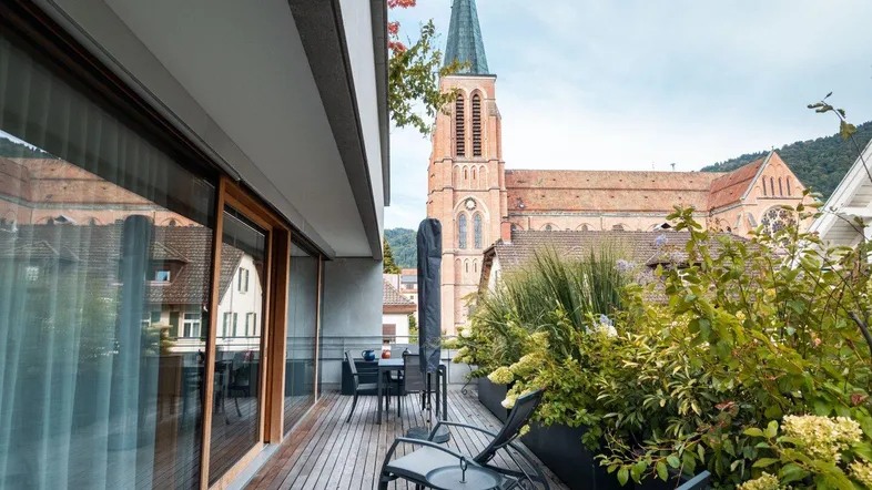 Große Holzterrasse mit Sitzgelegenheiten und Blick auf eine historische Kirche.