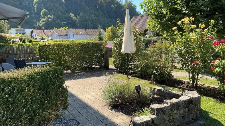 Sonniger Terrassenbereich mit Gartenmöbeln, umgeben von Hecken und Blumenbeeten.
