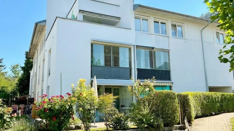 Modernes Mehrfamilienhaus mit weißer Fassade, großen Fenstern und gepflegtem Vorgarten.
