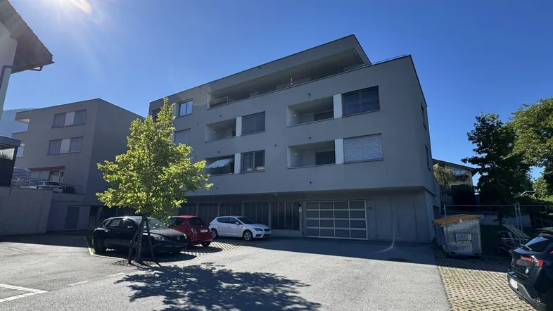 Modernes Mehrfamilienhaus mit Parkplätzen und Tiefgaragenzufahrt unter strahlend blauem Himmel.