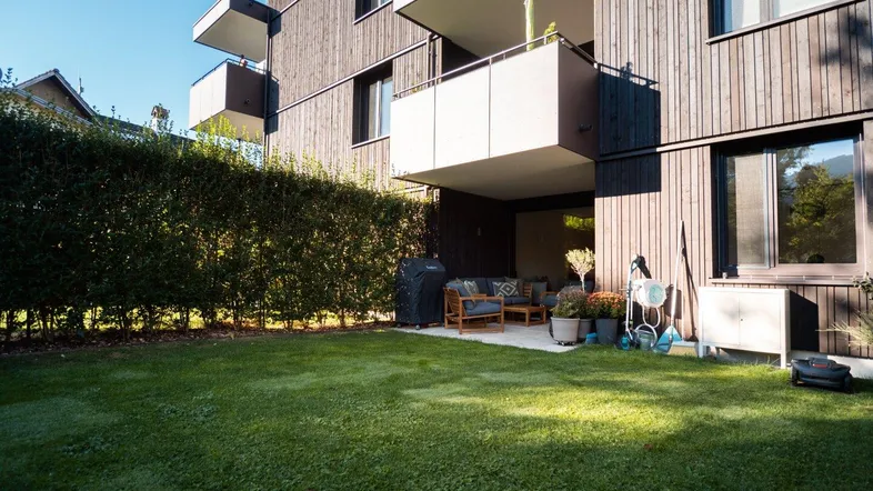 Moderner Gebäudekomplex mit gepflegtem Rasen und einer möblierten Terrasse im Erdgeschoss.