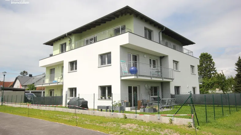 Modernes Mehrfamilienhaus mit weißer und grüner Fassade, umgeben von einer Grünfläche.