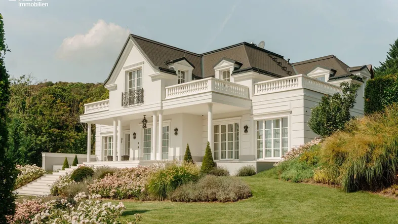 Elegante weiße Villa mit klassischer Architektur, umgeben von einem gepflegten Garten und blühenden Sträuchern.