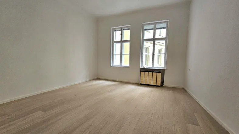 Heller, leerer Raum mit Holzboden und zwei Fenstern, bereit zur individuellen Gestaltung.