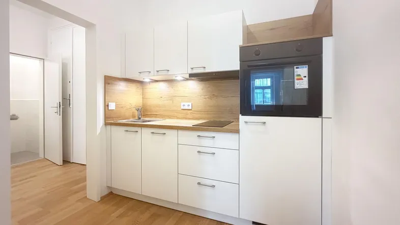 Moderne Einbauküche in Weiß mit Holzakzenten, integriertem Backofen und Kochfeld.