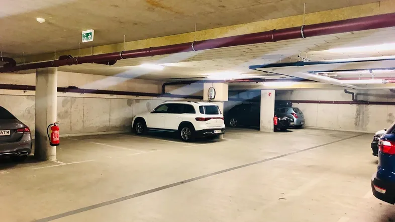 Geräumige Tiefgarage mit mehreren Stellplätzen, Betonwänden und sichtbaren Leitungen, gut beleuchtet.