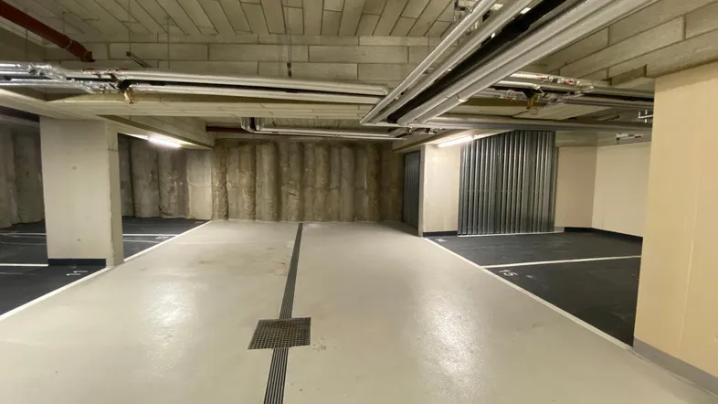 Geräumige Tiefgarage mit Betonwänden und -decken, gut beleuchtet und funktional gestaltet.