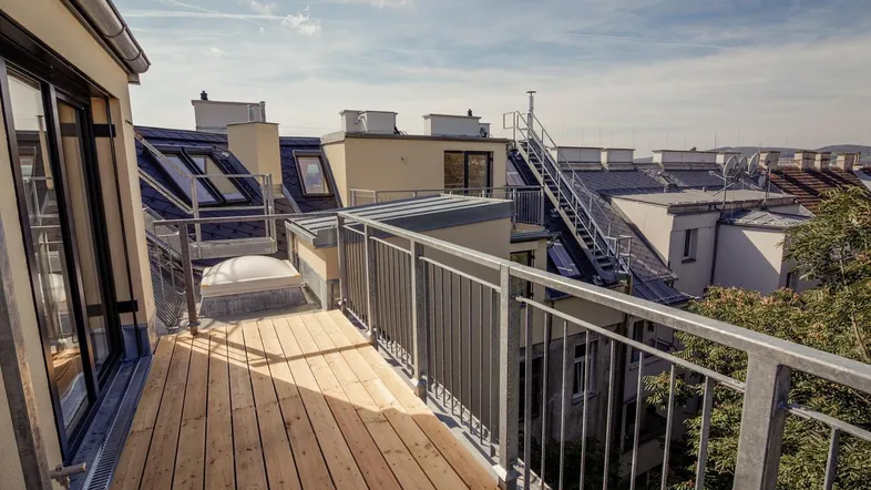 Geräumige Dachterrasse mit Holzboden und Metallgeländer, bietet einen weiten Blick über die Dächer der Stadt.
