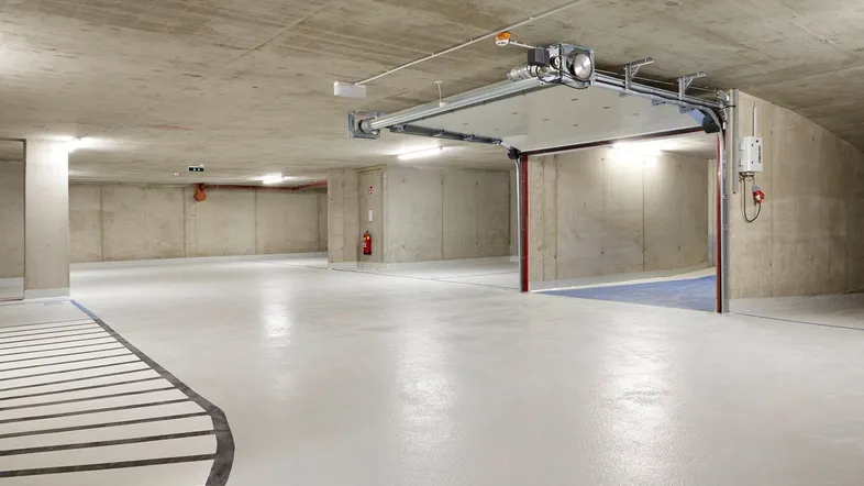 Geräumige Tiefgarage mit sauberem Betonboden und automatischem Garagentor, gut beleuchtet.