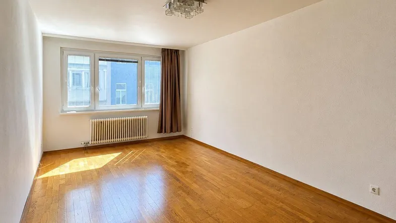 Helles Zimmer mit Holzparkettboden und großem Fenster, das viel Tageslicht hereinlässt.