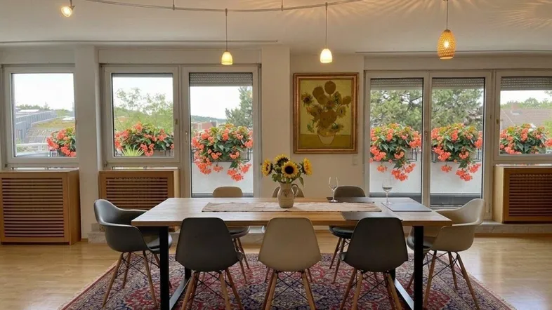 Heller Essbereich mit großem Holztisch, modernen Stühlen und Blick ins Grüne durch die Fenster.