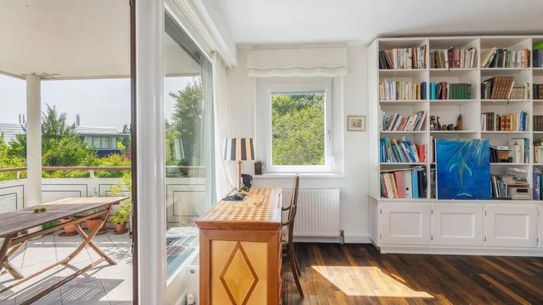 Heller Wohnbereich mit Holzboden, großem Bücherregal und Zugang zu einem sonnigen Balkon.