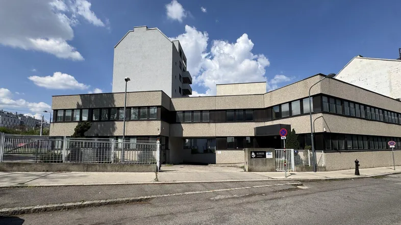 Mehrstöckiges Gebäude mit grauer Fassade und vielen Fenstern unter blauem Himmel.