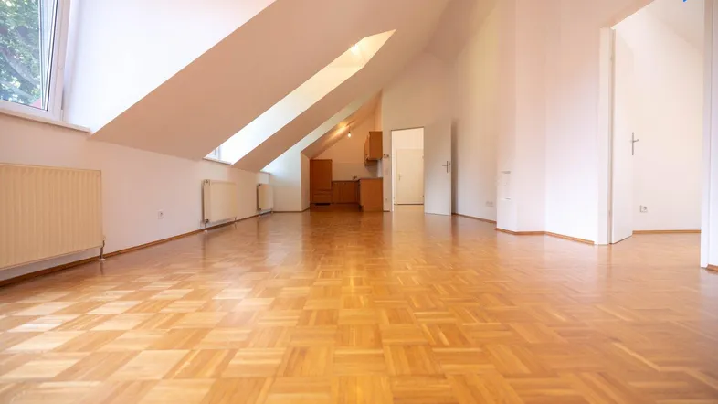 Offener Wohnbereich mit Parkettboden, Dachschrägen und Blick zur Küche und weiteren Räumen.