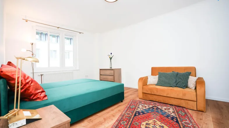 Helles Schlafzimmer mit Holzboden, einem bequemen Bett und einem kleinen Sofa.