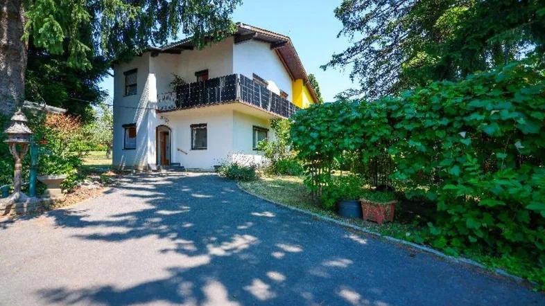 Einfamilienhaus mit weißer und gelber Fassade, umgeben von Bäumen und einem gepflasterten Weg.