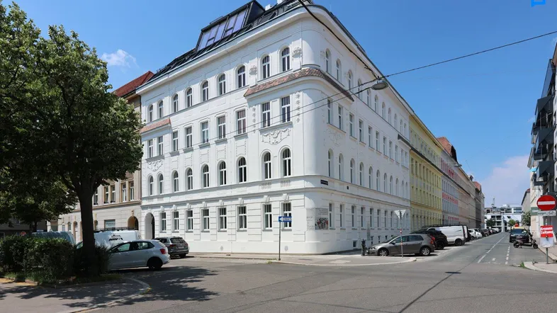 Eckgebäude mit frisch renovierter Fassade und modernem Dachausbau in urbaner Umgebung.