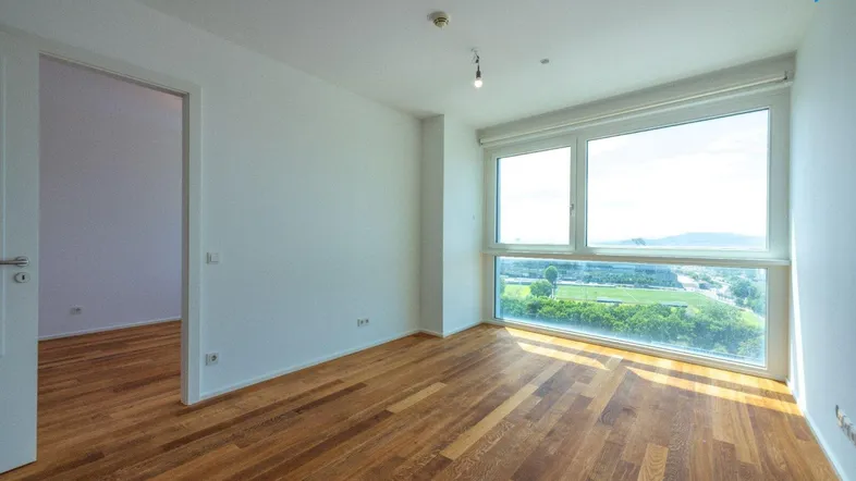 Helles Zimmer mit Holzboden und großen Fenstern, die einen weiten Blick nach draußen bieten.