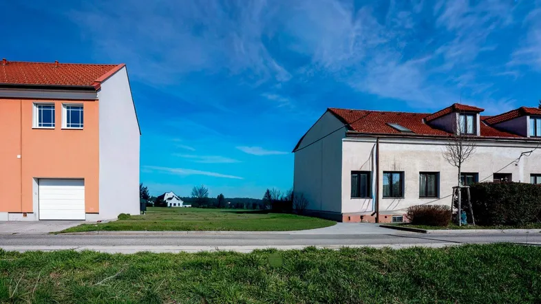 Zwei Häuser an einer Straße mit einem freien Grundstück dazwischen unter blauem Himmel.