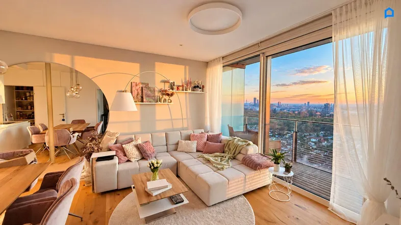 Helles Wohn- und Esszimmer mit Parkettboden, gemütlichem Sofa und weitem Stadtblick bei Sonnenuntergang.