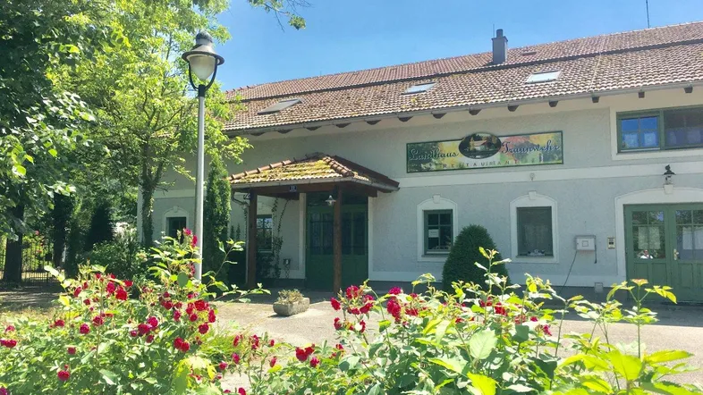 Vorderansicht eines Landhauses mit blühenden Rosensträuchern und einem gepflegten Vorgarten unter blauem Himmel.