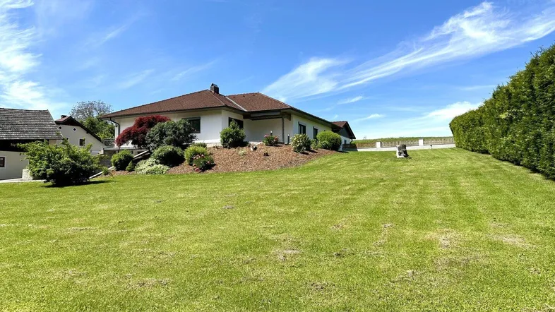 Großzügiger Gartenbereich mit weitläufiger Rasenfläche und Blick auf das Einfamilienhaus unter blauem Himmel.