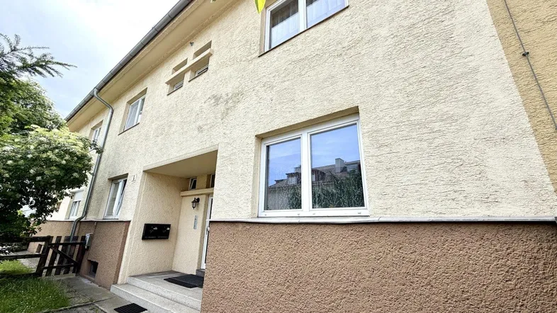 Vorderansicht eines Reihenhauses mit beiger Fassade und braunem Sockelbereich unter hellem Himmel.