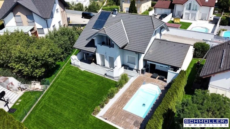 Luftaufnahme eines Einfamilienhauses mit großem Garten, Swimmingpool und Photovoltaikanlage auf dem Dach.