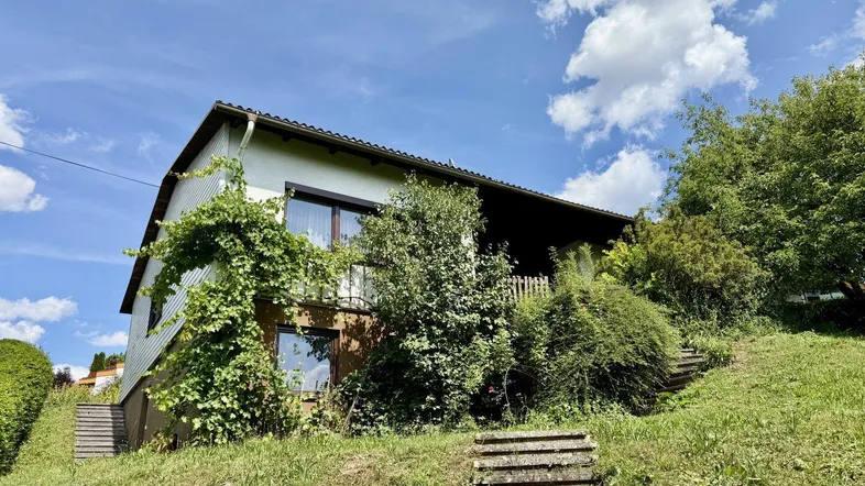 Das Haus ist in eine grüne Hanglage eingebettet, mit einer Treppe, die zum Eingang führt.