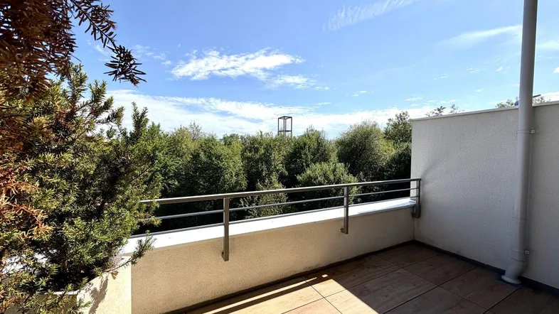 Geräumiger Balkon mit Holzboden und weitem Blick ins Grüne unter blauem Himmel.