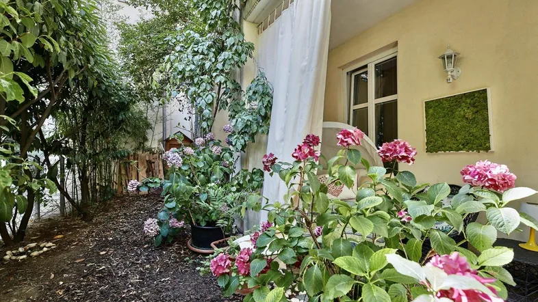 Grüner Gartenbereich mit blühenden Hortensien und einem kleinen gepflasterten Sitzbereich am Haus.