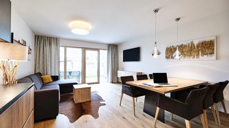 Helles Wohn- und Esszimmer mit Holzboden, modernem Sofa und Zugang zur Terrasse.