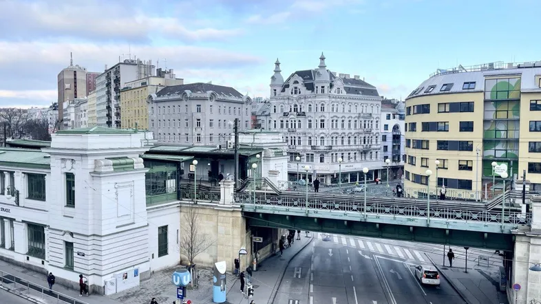Panoramablick auf eine belebte Stadtstraße mit historischer Architektur und einer erhöhten Brücke.