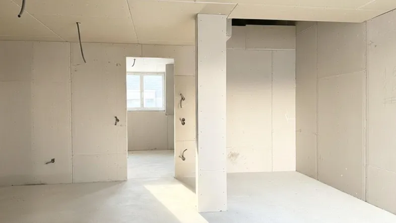 Unfertiger Innenraum mit Trockenbauwänden und Betonboden, bereit für den weiteren Ausbau.