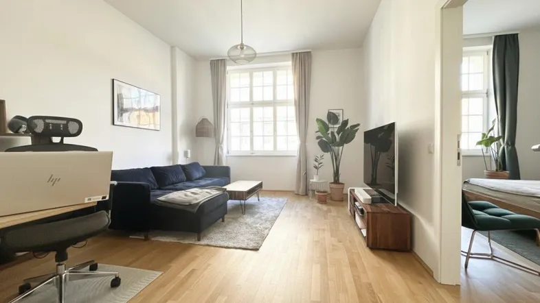 Helles Wohnzimmer mit Holzboden, bequemer Couch und Arbeitsbereich am Fenster, modern eingerichtet.