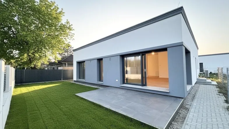 Modernes Einfamilienhaus mit gepflegtem Rasen und einer gefliesten Terrasse im Freien.