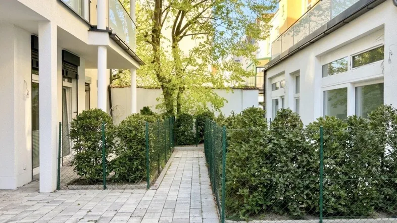 Gepflasterter Innenhof zwischen Gebäuden mit grünen Hecken und einem Zugangsweg.