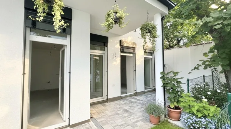 Gepflasterte Terrasse mit Grünflächen und hängenden Pflanzen, direkt zugänglich von mehreren Räumen.
