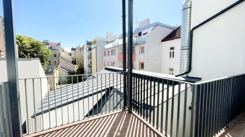 Heller Balkon mit Holzboden und Metallgeländer, bietet einen Blick auf die umliegenden Gebäude.