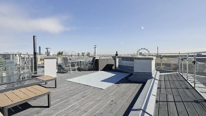 Geräumige Dachterrasse mit Holzbelag, Sitzgelegenheiten und weitem Blick über die Stadt.