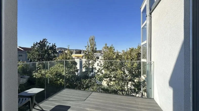 Moderner Balkon mit Glasgeländer und Holzboden, bietet einen schönen Blick ins Grüne.