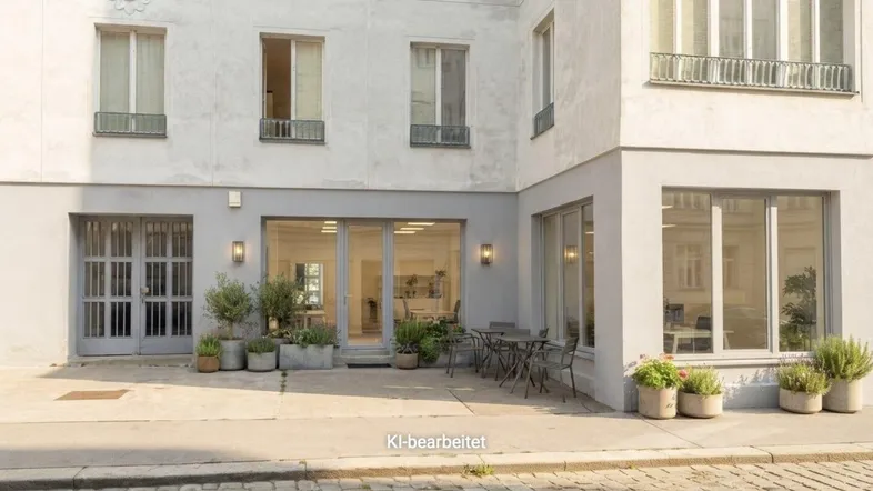 Außenansicht eines Geschäftsgebäudes mit kleiner Terrasse und Sitzgelegenheiten an einer gepflasterten Straße.
