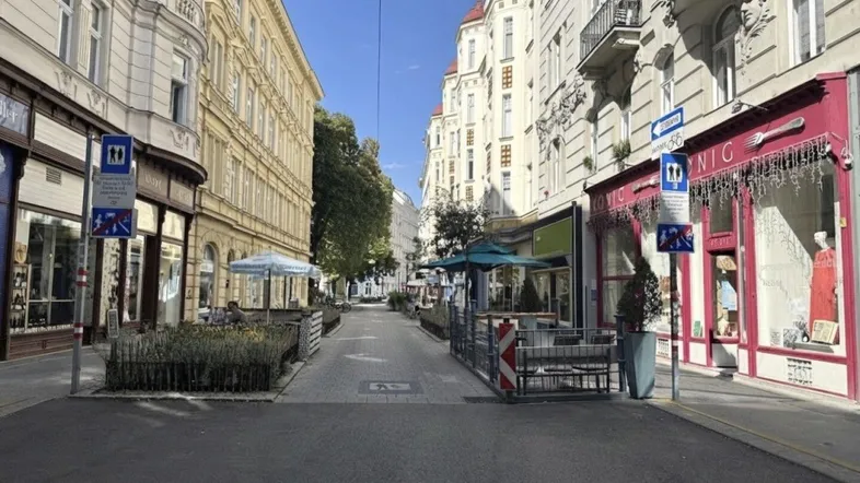 Eine belebte Straße mit historischen Gebäuden, Geschäften und Außengastronomie unter blauem Himmel.