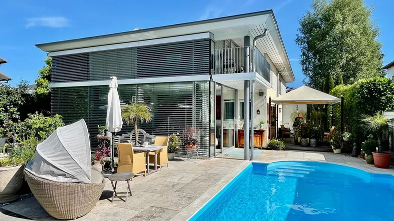 Modernes Haus mit großem Pool, sonniger Terrasse und gemütlichen Sitzbereichen im Garten.