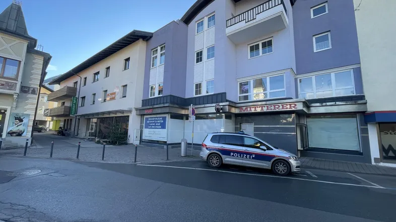Gebäudeansicht von der Straße mit Geschäften im Erdgeschoss und Wohnungen darüber, sowie einem Polizeifahrzeug.